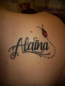 Фото тату божьей коровки с именем 'Alaina', выполненное в черном цвете. Рисунок выглядит стильно и персонализированно.