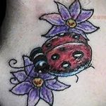 Фото тату божьей коровки среди фиолетовых цветов на боку. Яркий и красочный рисунок татуировки.