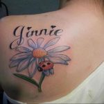 Фото татуировки цветка ромашки с божьей коровкой и надписью 'Jinnie' на спине. Красивый и персонализированный дизайн.
