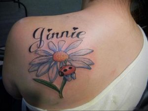 Фото татуировки цветка ромашки с божьей коровкой и надписью 'Jinnie' на спине. Красивый и персонализированный дизайн.
