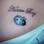 Фото тату с изображением синей и черной божьей коровки и надписью 'Hunter Bug' выполненной красивым шрифтом. Оригинальный и персонализированный рисунок.
