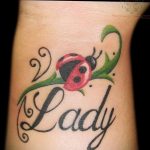 Фото тату божьей коровки, сидящей на зеленом стебле с надписью "Lady". Красивый и оригинальный рисунок татуировки.