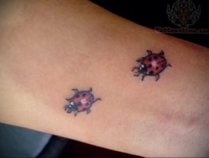 Фото двух маленьких татуировок божьих коровок, расположенных на руке. Простой и минималистичный дизайн.
