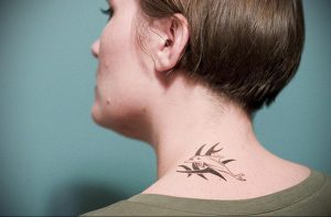 Фото минималистичной татуировки ветки с листьями на затылке. Изображение выполнено тонкими черными линиями, создающими элегантный и изящный вид.