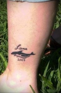 Фото тату дельфина с надписью 'Luna' и датой '2009'. Татуировка выполнена в черном цвете.