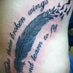 Фото тату на руке с изображением пера, летящих птиц и надписи 'Take these broken wings and learn to fly'. Черно-белая графика, мотивационный смысл.