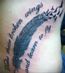 Фото тату на руке с изображением пера, летящих птиц и надписи 'Take these broken wings and learn to fly'. Черно-белая графика, мотивационный смысл.