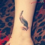 Фото тату на лодыжке: черное перо и буква 'X', выполненные в минималистичном стиле. Нежный и стильный рисунок татуировки.