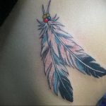 Фото тату: красочное перо в стиле Native American, украшенное бусинами, расположено на боку. Яркие цвета и этнические мотивы.