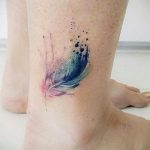 Фото акварельной татуировки пера на женской лодыжке. Нежные переходы розовых и голубых оттенков создают эффект легкости и воздушности.