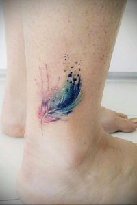 Фото акварельной татуировки пера на женской лодыжке. Нежные переходы розовых и голубых оттенков создают эффект легкости и воздушности.
