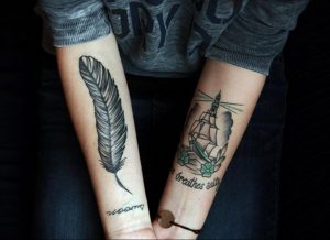 Фото парных татуировок на предплечьях: одно изображение пера, другое - корабля и маяка. Черно-белые рисунки.