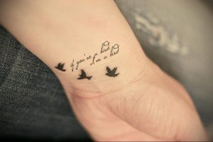 Фото тату: две маленькие птицы и надпись 'if you’re a bird I’m a bird' на запястье. Минимализм, каллиграфия, нежный дизайн.