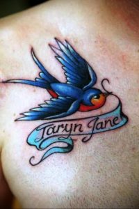 Фото тату: ласточка в стиле олд скул с надписью 'Taryn Jane' на ленте. Яркие цвета, четкие контуры, традиционный стиль.