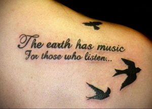Фото тату с надписью "The earth has music for those who listen..." и силуэтами летящих птиц на лопатке.
