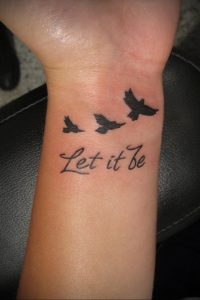 Фото тату на запястье с изображением трех летящих птиц и надписи "Let it be". Черно-белый рисунок татуировки выполнен в минималистичном стиле.