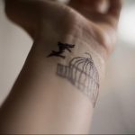 Фото тату: небольшая черно-белая татуировка птицы, вылетающей из клетки, на женском запястье. Простой и элегантный рисунок татуировки.