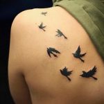 Фото тату на плече с изображением нескольких маленьких летящих ласточек. Рисунок выполнен в черных тонах.