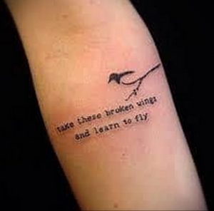 Фото тату: черная птица с надписью "Take these broken wings and learn to fly". Татуировка символизирует преодоление трудностей и стремление к возрождению.
