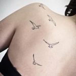 Фото минималистичных татуировок с изображением летящих птиц на спине. Тонкие линии и лаконичный дизайн создают ощущение легкости и свободы.