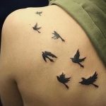 Фото тату: маленькие черные птицы, летящие по коже спины. Минималистичный рисунок татуировки, выполненный в графичном стиле.