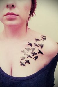 Фото татуировки стаи летящих птиц на ключице и груди. Черно-белый рисунок, минималистичный стиль, изящный дизайн.