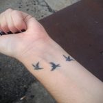 Фото нескольких миниатюрных татуировок птиц на запястье. Черно-белый рисунок, минималистичный стиль, нежный дизайн.
