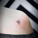 Фото минималистичной татуировки ласточки на плече. Тонкие черные линии создают изящный силуэт птицы.