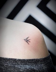 Фото минималистичной татуировки ласточки на плече. Тонкие черные линии создают изящный силуэт птицы.