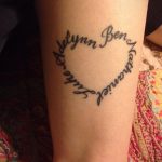 Фото тату на предплечье: сердце, образованное именами 'Adelynn', 'Luke', 'Ben' и 'Katharine'. Черно-белый рисунок татуировки.