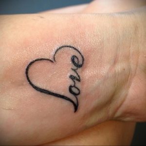 Фото тату с надписью 'Love' внутри контура сердца на запястье. Простой и элегантный рисунок татуировки, символизирующий любовь.