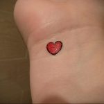 Фото тату на запястье: крошечное красное сердце, выполненное в простом стиле. Небольшой и аккуратный рисунок татуировки.