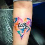 Фото тату: красочное сердце, выполненное в технике акварели, с надписью 'Lilly' и датой рождения. Идеальный эскиз тату для памятного рисунка.