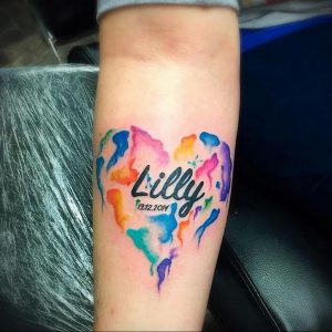 Фото тату: красочное сердце, выполненное в технике акварели, с надписью 'Lilly' и датой рождения. Идеальный эскиз тату для памятного рисунка.