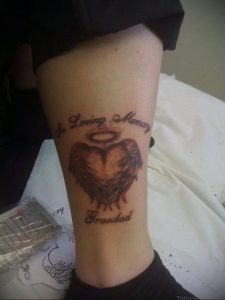 Фото тату сердца с крыльями и надписью "In Loving Memory Grandad". Татуировка на ноге, выполненная в ярких цветах.