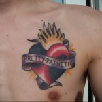 Фото тату горящего сердца с надписью 'Pretty Pathetic' на груди. Яркий и драматичный рисунок татуировки, символизирующий боль, страсть и разочарование.