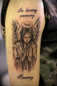 Фото тату ангела на плече с надписью 'In loving memory' и именем 'Sammy'. Черно-белый рисунок татуировки в стиле реализм.
