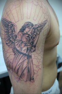 Фото тату ангела, склонившего голову в молитве на руке. Татуировка выполнена в черно-серых тонах с использованием тонких линий.