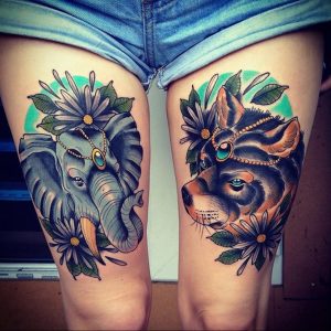 Фото тату слона и волка на бедрах. Оба животных изображены в стиле олдскул, с цветочными венками и яркими цветами.