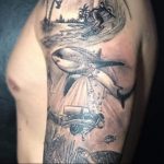 Фото тату: реалистичное изображение акулы и дайвера под водой на руке. Детализированный рисунок татуировки с пузырьками и морскими растениями.