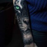 Фото татуировки на предплечье: реалистичное изображение головы тигра с зелеными глазами. Яркие цвета и детализированная проработка.
