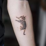 Фото тату реалистичного котенка в прыжке на предплечье. Детализированный рисунок с проработанной шерстью и выразительными глазами. Черно-серые тона.