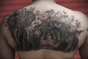 Фото татуировки на спине с изображением семьи слонов, выполненной в черно-серых тонах с эффектом дымки.
