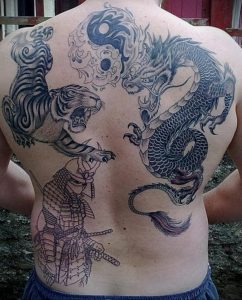 Фотография большой татуировки на спине, изображающей тигра, дракона, самурая и символ Инь-Янь. Черно-серый рисунок с множеством деталей.