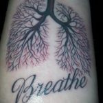 Фото тату: реалистичное изображение легких с надписью "Breathe" на руке. Рисунок татуировки в черно-белом стиле с добавлением красных акцентов.