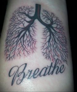 Фото тату: реалистичное изображение легких с надписью "Breathe" на руке. Рисунок татуировки в черно-белом стиле с добавлением красных акцентов.
