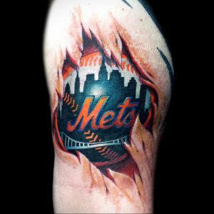 Фото тату с логотипом бейсбольной команды New York Mets, выполненным в ярких цветах на плече. Детализированный рисунок татуировки с изображением логотипа и городского пейзажа.