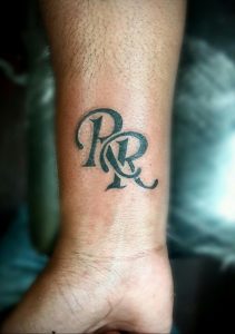 Фото тату с монограммой из двух букв 'P' и 'R', выполненной в черном цвете на запястье. Элегантный и минималистичный рисунок татуировки.