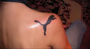 Фотография черной татуировки на плече, изображающей логотип Puma – прыгающего хищника. Минималистичный дизайн.