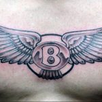 Черно-серое фото татуировки на груди с изображением буквы 'B' в круге, окруженной расправленными крыльями. Детализированный рисунок, выполненный в реалистичном стиле.
